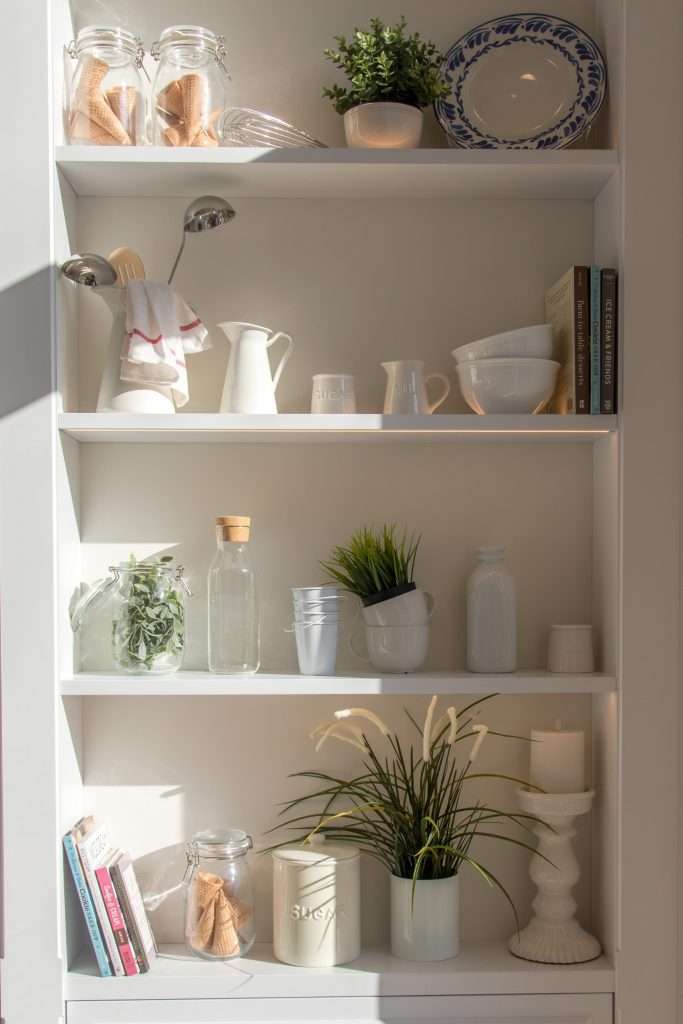 White ceramic bowls and bottles along with other glassware perfectly arranged on the pantry.
